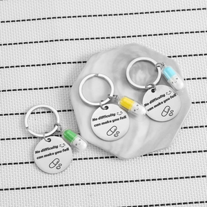 Three pill-shaped keychains with motivational tags and faces on a marble tray