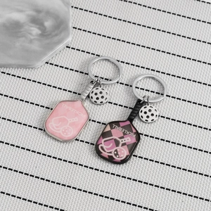 Close-up of pink and black pickleball paddle keychains with miniature balls on stone