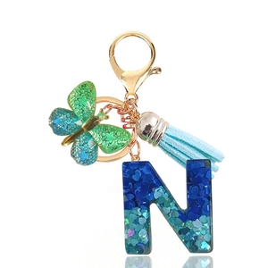 Detail of blue resin letter N keychain with heart sequins, teal butterfly and tassel