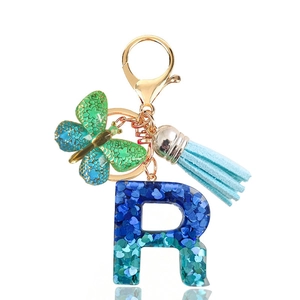 Macro shot of glitter resin letter R keychain with teal butterfly and blue suede tassel