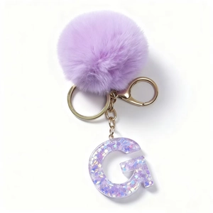 Dettaglio di un pompon viola in finta pelliccia e portachiavi lettera G con glitter