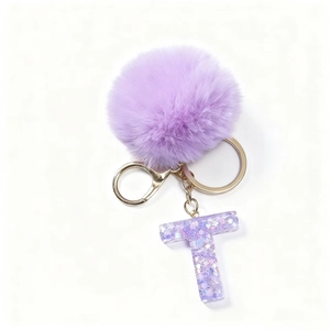 Dettaglio portachiavi con lettera T in resina viola, pompon morbido e anello dorato