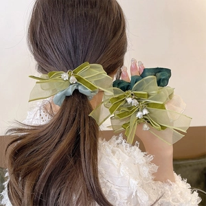 Dettaglio di elastico verde con fiocco di velluto e ciondoli di mughetto bianco sui capelli