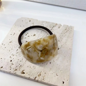 Detailed macro view of an amber-textured acetate hair ring on a neutral stone base