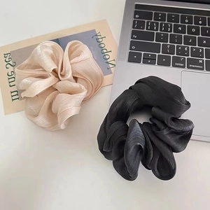 Detail of satin scrunchies in champagne and black colors on a white desktop