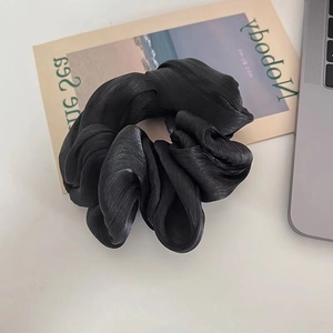 Close-up of black satin scrunchie featuring high-density pleated texture and silk-like gloss