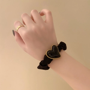 Detailed shot of black scrunchie with a gold-trimmed heart charm worn on the wrist