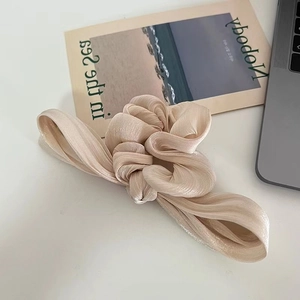 Close-up of champagne satin scrunchie with soft silk texture and elegant pleated design