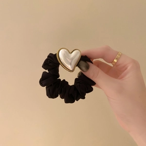Detail of a black velvet scrunchie featuring a white pearl heart with a gold trim finish