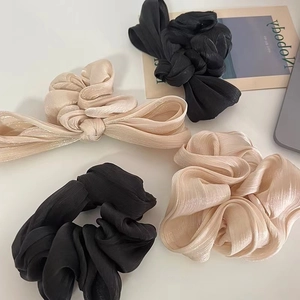 Close-up of pleated satin scrunchies with bow design in black and champagne gold
