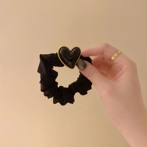Detailed view of a black satin scrunchie with a gold-bordered heart charm held by hand