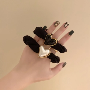 Detail of vintage heart charms on a black elastic scrunchie worn on a wrist