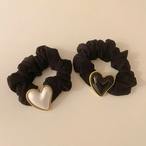 Detail of two black scrunchies with white and black gold-rimmed heart charms on beige base