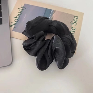 Elegant black pleated satin scrunchie with a glossy finish shown on an aesthetic background