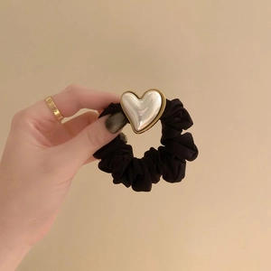 Elegant black scrunchie with vintage pearl heart pendant held in hand on beige background