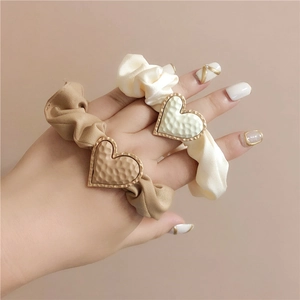 Detail of cream and khaki matte scrunchies with hammered metal heart charm on wrist