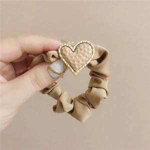 Close-up of khaki scrunchie featuring a hammered metallic heart charm with gold trim