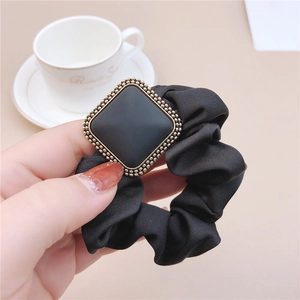 Close-up of black satin scrunchie featuring a golden square metallic heart charm on a soft fabric