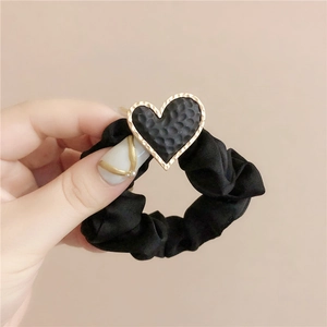 Close-up of black matte scrunchie with a gold-bordered heart charm and hammered texture