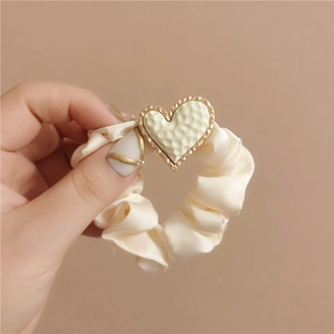 Detail of cream satin scrunchie featuring a gold textured heart charm accessory