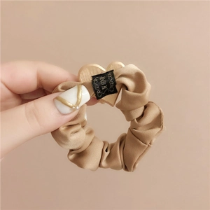 Elegant beige satin scrunchie with golden heart charm and matte texture for women