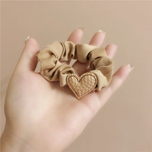 Matte beige scrunchie with a gold heart pendant charm in a textured hammered finish