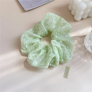 Gros plan d'un chouchou vert clair en tissu plissé sur un bureau au style minimaliste