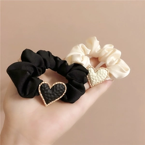 Detail of matte heart charms on satin scrunchies in black and cream white colors