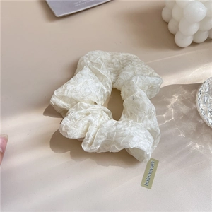 Détail d'un chouchou blanc cassé à texture froncée avec une étiquette de marque latérale