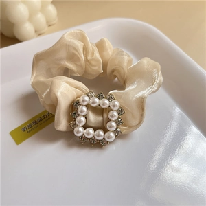 Detailed close-up of a cream-colored satin scrunchie with elegant pearl and rhinestone inlay