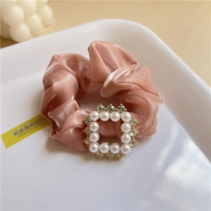 Macro detail of a pink satin scrunchie featuring a luxury pearl and rhinestone square buckle