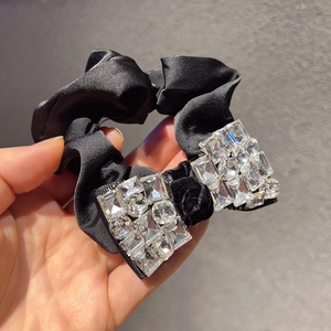 Détail d'un chouchou en satin noir orné d'un double nœud luxueux serti de strass