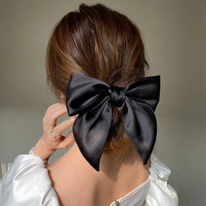 Detail of elegant black satin oversized bow hair tie worn on a low ponytail
