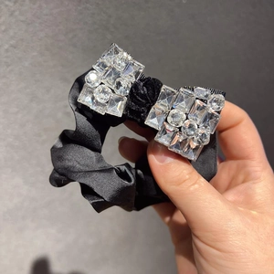 Chouchou élégant en satin noir avec un nœud en strass étincelants tenu à la main