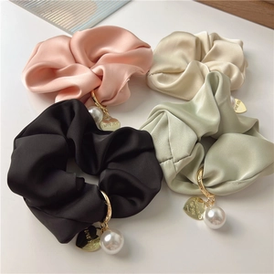 Detail of four satin scrunchies with large pearls and heart pendants on light surface