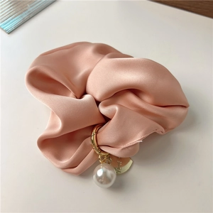 Detail of pink satin scrunchie with pearl pendant and heart charm on silk fabric