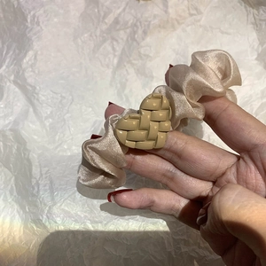 Close-up of champagne satin scrunchie with a beige woven heart-shaped charm detail