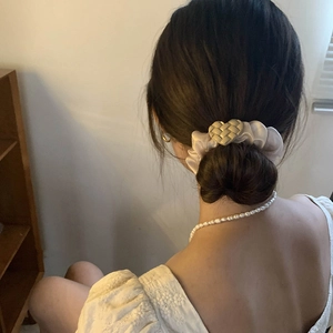 Close-up of cream fabric scrunchie with heart charm on a bun and pearl necklace accessory