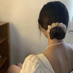 Detail showing cream satin scrunchie with woven heart charm used for high bun styling