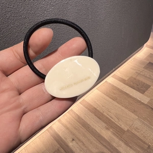 Detailansicht eines schwarzen elastischen Haargummis mit cremefarbenem Anhänger und Logo