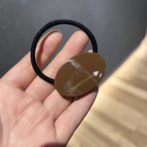 Nahaufnahme eines elastischen Haargummis mit braunem Acrylelement und goldener Schrift