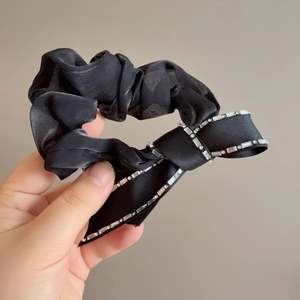 Black satin scrunchie with sparkling rhinestone bow held by hand on neutral background