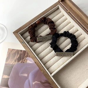 Close-up of brown and black fabric hair scrunchies with engraved CHANCE metal charms