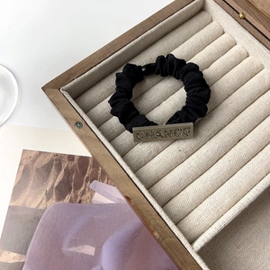 Close-up of black pleated hair tie with 'CHANCE' engraved rhinestone metal plate