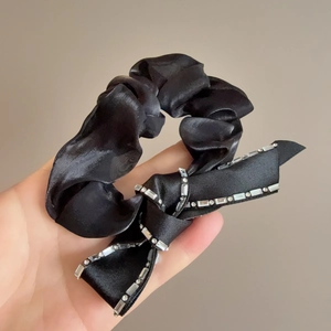 Close-up of black satin scrunchie featuring a sparkling rhinestone-edged ribbon bow