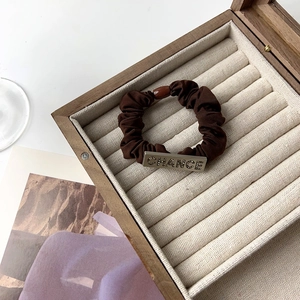 Close-up of dark brown pleated scrunchie with a rectangle metal plate engraved with CHANCE
