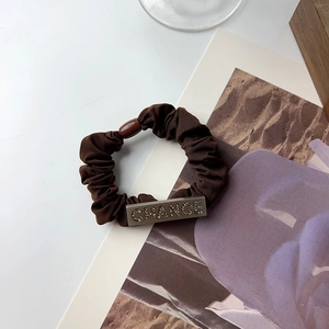 Detailed macro view of coffee satin hair scrunchie with crystal CHANCE metal plate