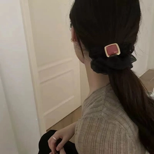 Detailansicht eines schwarzen Netzhairbands mit rubinartigem Akzent auf einem Zopf