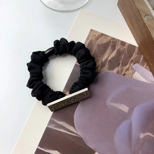 Macro detail of black silk hair tie featuring a silver metal plate with rhinestone letters