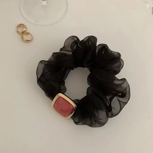 Detail eines schwarzen Organza-Haargummis mit einem roten quadratischen Anhänger